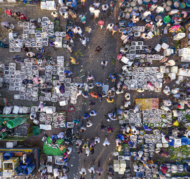Aerial view of a bustling fish market with numerous fishermen and traders sorting fresh catch in crates across the busy ground in Chattogram, Chittagong Division, Bangladesh.
