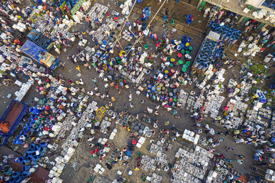 Aerial view of a bustling fish market with numerous people, colorful crates, blue barrels, and trucks in Chattogram, Chittagong Division, Bangladesh.
