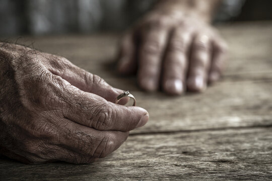 A pair of hands on a wooden table; one hand is removing a wedding ring, concept for couple problems.