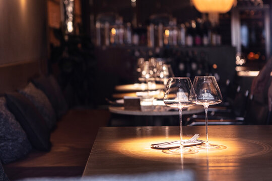 Atmospheric table setting in restaurant: two empty wine glasses in warm lighting. Premium bar or restaurant. There are two elegant transparent wine glasses on wooden table