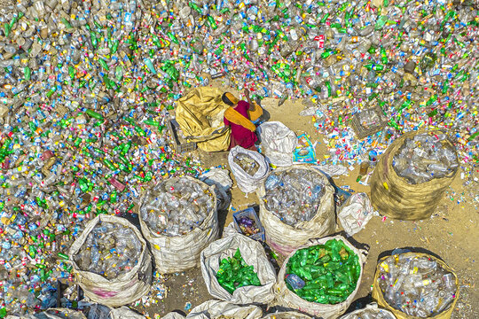 Aerial view of a worker sorting through a vast collection of discarded plastic bottles in large bags at a recycling facility in Chattogram, Chittagong Division, Bangladesh.