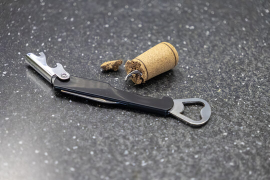 A broken wine cork is stuck on a metallic corkscrew tool, highlighting a failed service or common kitchen mishap during beverage preparation on a dark granite surface for restaurants
