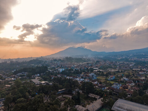 Aerial view of Cihideung with residential houses, lush greenery, and a mountain backdrop under a dramatic sunset sky in Parongpong, West Java, Indonesia.