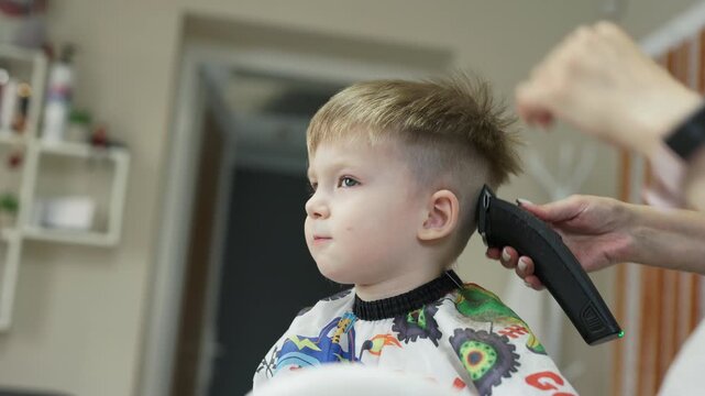 Boy getting a haircut with hair clipper at childrens barbershop