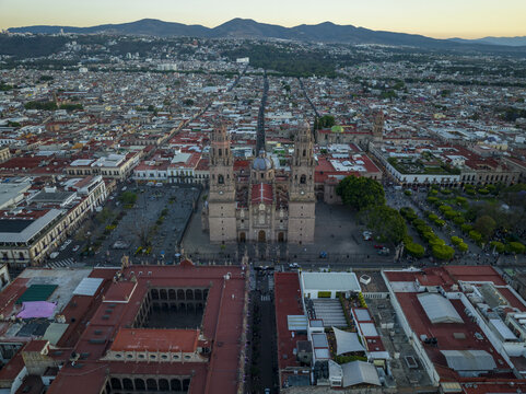 Aerial view of Morelia Cathedral and Plaza de Armas surrounded by historic colonial rooftops and urban landscape at sunset in Morelia, Michoacan, Mexico.