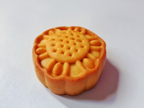 High-angle closeup of a golden baked flower-patterned mooncake isolated on a plain white surface