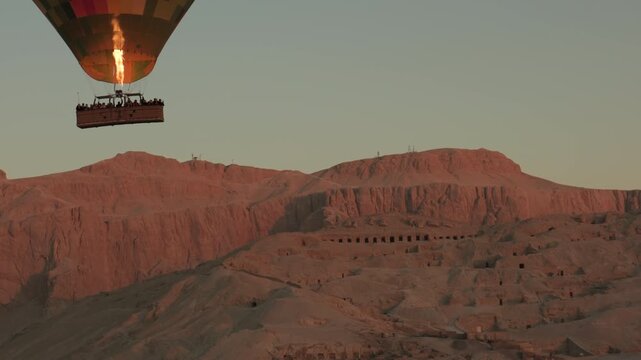 Morning hot air balloon ride in Luxor, flying over semi-rocky Deir el-Bahari complex of ancient Egyptian buildings Temple of Hatshepsut