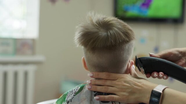 Little boy getting a haircut with hair clipper at childrens barbershop, back view
