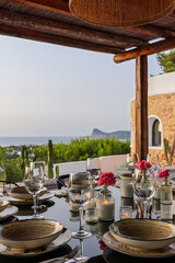 Fototapeta premium Candlelit dinner table sits in view on Ibiza, Spain with wine glasses, lit by warm twilight illumination and visible candle glow.