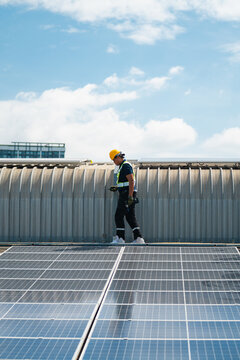 Solar electricity power technology for sustainable energy, Solar panel technician, rooftop, worker, hard hat, safety harness, renewable energy maintenance at industrial site under blue sky