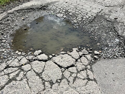 Large pothole filled with rainwater on badly cracked asphalt road showing damaged pavement surface