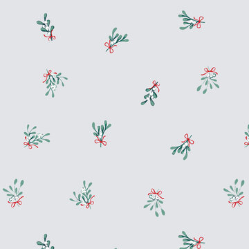 Delicate mistletoe sprigs with red bows scattered across a soft grey background for festive holiday design