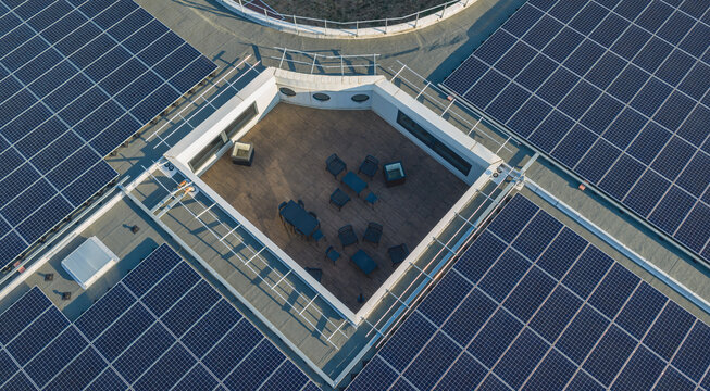 Aerial view of a rooftop terrace with wooden deck and furniture surrounded by solar panel arrays on a modern commercial building in Livron-sur-Drome, Auvergne-Rhone-Alpes, France.