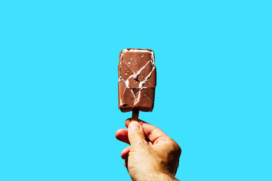 Hand Holding Chocolate Ice Cream Bar on Blue Background