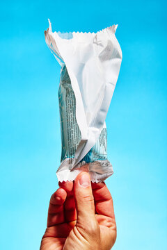 Hand holding an opened snack wrapper against a blue background