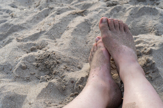 Close-up of sandy feet resting on beach sand, relaxed summer lifestyle photo with copy space.