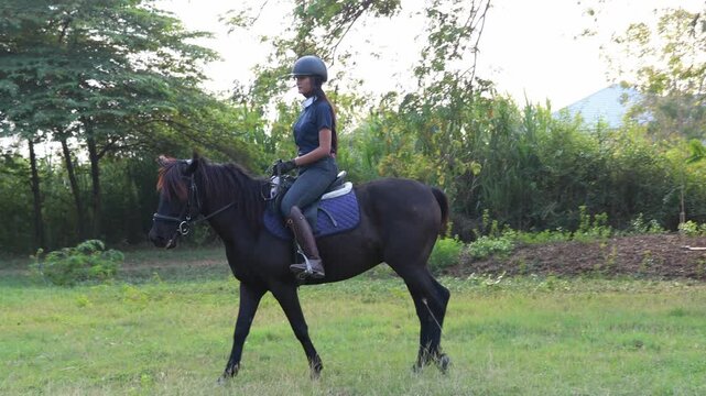 Asian female equestrian athletes coaches wearing helmets practical attire practice outdoor training ground jogging slowly across the grass evening familiarizing themselves horses  graceful movements.