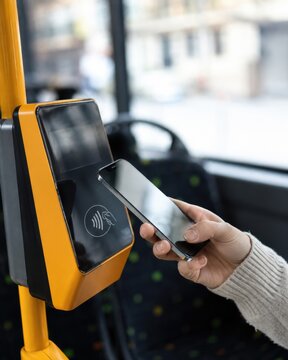 Passenger paying for ride using smartphone NFC contactless technology at yellow electronic validator in public transport. Smart ticketing, wireless payment, and urban mobility concept
