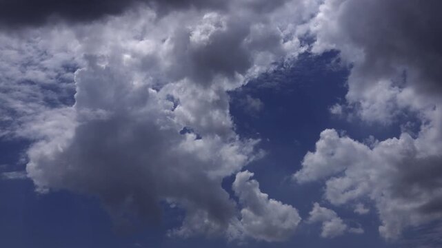 Time-lapse of towering white cumulus clouds drifting across a deep blue sky.