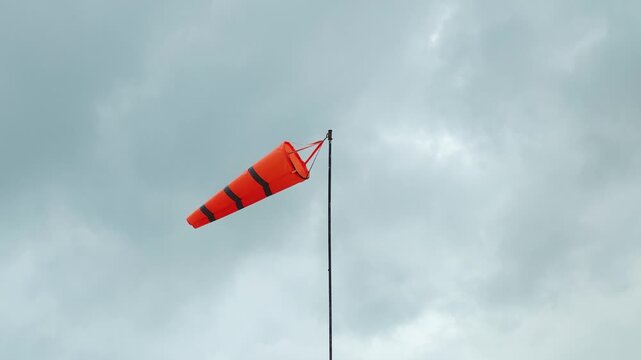 An orange with reflection stripe windsock on cloudy sky before storm coming weather. The equipment using to indication windy speed and direction.