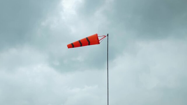 An orange with reflection stripe windsock on cloudy sky before storm coming weather. The equipment using to indication windy speed and direction.