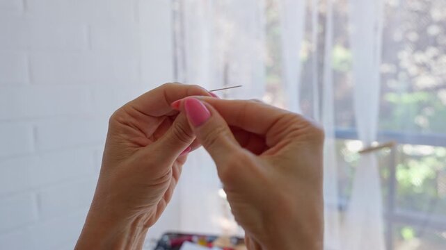 Woman hands with pink nails threading a needle at home
