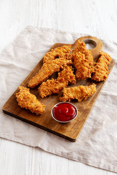Organic Crispy Chicken Strips with Ketchup on a Wooden Board, side view.
