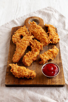 Organic Crispy Chicken Strips with Ketchup on a Wooden Board, side view.