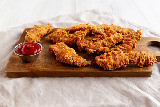 Organic Crispy Chicken Strips with Ketchup on a Wooden Board, side view.