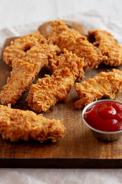 Organic Crispy Chicken Strips with Ketchup on a Wooden Board, side view.