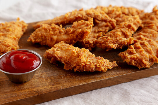 Organic Crispy Chicken Strips with Ketchup on a Wooden Board, side view.