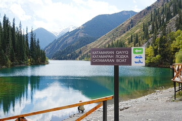 Information signpost for boat rentals at Kolsai Lake with turquoise water and mountain view © 현주 정