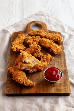 Organic Crispy Chicken Strips with Ketchup on a Wooden Board, side view.