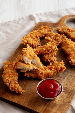 Organic Crispy Chicken Strips with Ketchup on a Wooden Board, side view.