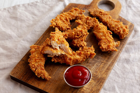 Organic Crispy Chicken Strips with Ketchup on a Wooden Board, side view.