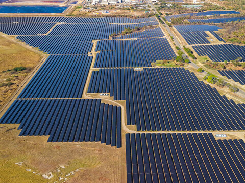 Aerial view of the Sun Metals Corporation solar farm featuring rows of photovoltaic panels in a dry landscape with an industrial facility in the background in Stuart, Queensland, Australia.
