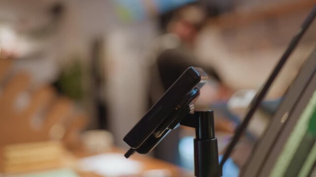 Closeup card reader at cafe counter, blurred barista in background, warm ambient light, wooden countertop and menu boards, modern terminal idle awaiting transaction, shallow depth of field, cozy