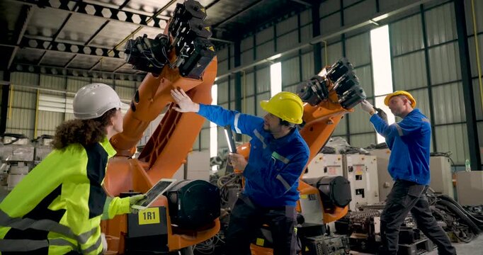 Engineering team inspects industrial robotic arms in factory workshop, using tablet and flashlight while checking mechanical components and coordinating maintenance for automated manufacturing.