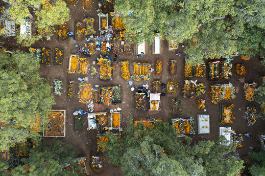 Aerial view of Tzintzuntzan graveyard decorated with vibrant orange marigold flowers for Day of the Dead celebrations with people visiting graves in Tzintzuntzan, Michoacan, Mexico.