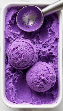 Two scoops of vibrant purple ube ice cream in a white container with an ice cream scoop