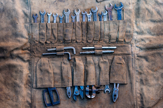 Vintage tool roll organizer with old wrenches and pliers, closeup. Flat lay macro shot of weathered canvas tool roll organizer filled with various old metal wrenches spanners Allen keys and pliers