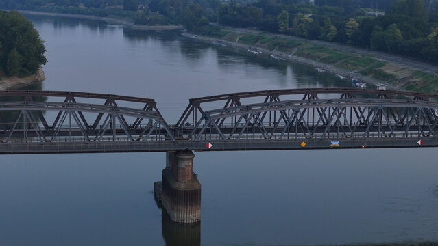 Aerial view of the metal truss bridge over the Po River during a summer heatwave with low water levels and hazy sunrise light in Cremona, Lombardy, Italy.