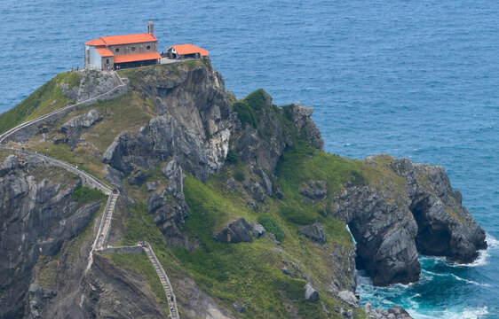 visitors exploring gaztelugatxe island with church and stairs leading to it in a peaceful and adventurous setting above rocky cliffs and blue ocean waters with green vegetation.