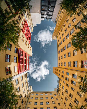 Dramatic upward view of yellow and red Berlin apartment buildings with spiral staircase and blue sky between facades
