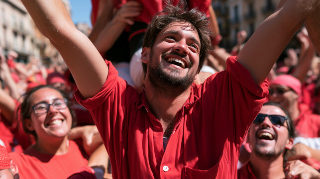 A joyful man celebrating during the Castells de Tarragona human tower festival wearing traditional red clothes under bright sunny daylight