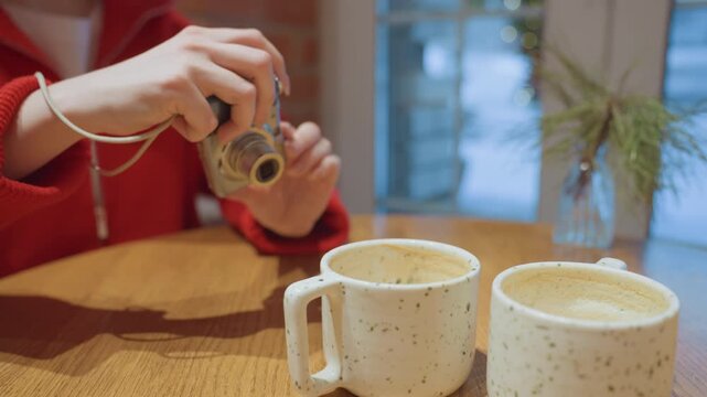 Indoor scene with woman taking pictures of mugs. Woman in red sweater capturing images of ceramic cups indoors. Cozy indoor setting with woman photographing speckled ceramic mugs at cafe table