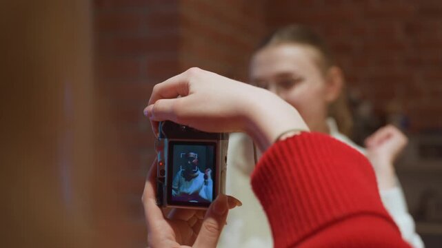 White woman in cafe posing for camera held by friend, redsleeved hands framing display, vintage camera screen showing portrait, relaxed smile, model test shoot, content creator rehearsal, lifestyle