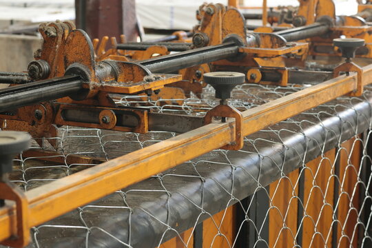 Industrial machine producing steel wire mesh in a metal factory, close-up of mechanical rollers and guides shaping galvanized wire