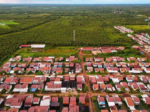 Aerial view of a residential neighborhood with rows of houses featuring red roofs, surrounded by lush green vegetation and trees in Barito Kuala Regency, South Kalimantan, Indonesia.