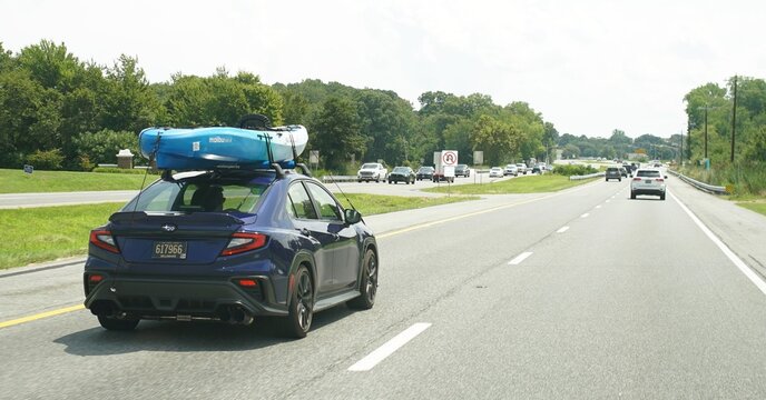 Sussex County, Delaware, U.S.A - Aug 1, 2025 - Blue Subaru WRX carrying a Malibu Two XL kayak on its roof while driving on Route 1 South towards the beach